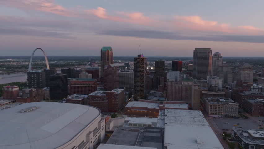 Aerial view of St. Louis at dusk, featuring the iconic gateway arch and downtown skyline against a vibrant evening sky, showcasing urban beauty and architectural landmarks