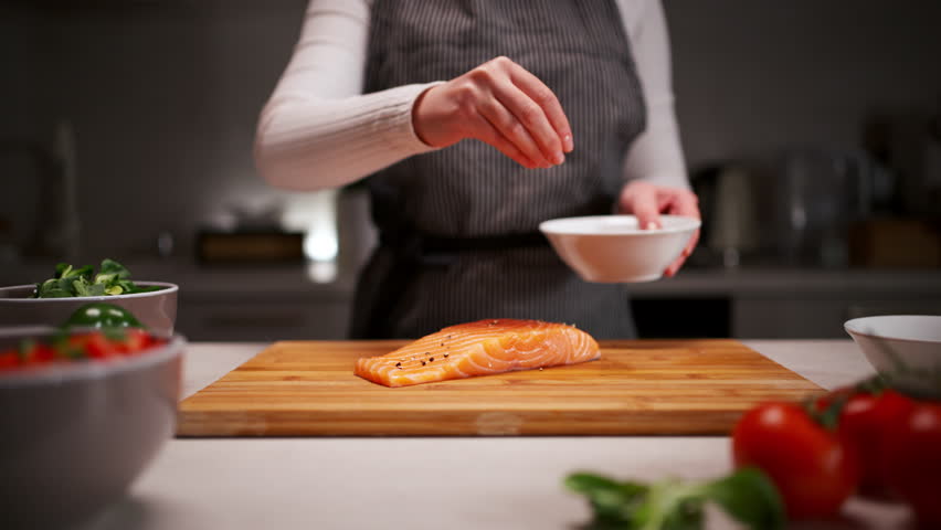 Woman chef preparing fresh salmon fish, sprinkling salt with the ingredients