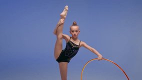 Caucasian little girl child kid daughter schoolgirl gymnast athlete dancer ballerina acrobat stand in split position flexibility artistic gymnastics spinning hoop sport event studio blue background - Powered by Shutterstock - Get 15% off with code: PIKWIZARD15