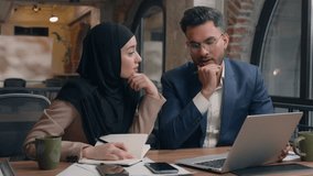 Two business colleagues co-workers talk discuss corporate work at office cafe multiracial male female employees Indian man muslim woman in hijab diverse businesswoman businessman write tasks laptop - Powered by Shutterstock - Get 15% off with code: PIKWIZARD15