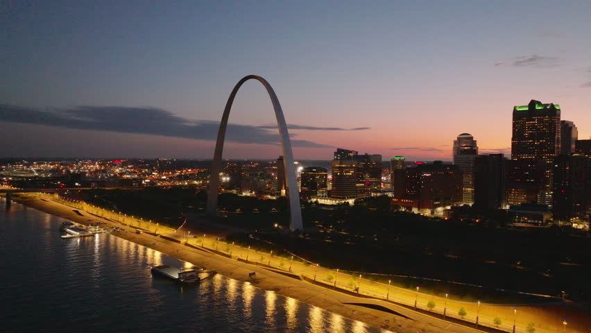 Aerial view of St. Louis at sunset, featuring the iconic gateway arch and city skyline. Luminous reflections on the water of Mississippi River create a picturesque scene