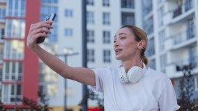 Positive caucasian woman waving hello during online video call through modern smartphone outdoors. Happy female having pleasant conversation with friends near contemporary building interior. - Powered by Shutterstock - Get 15% off with code: PIKWIZARD15