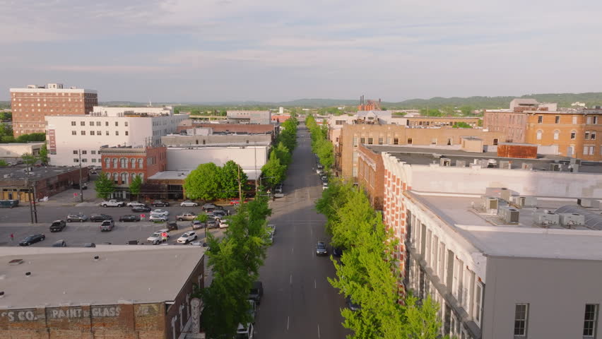 Aerial view of the streets of an American city. Historic buildings, treelined roads, and parked vehicles on a clear day while car drives on the road