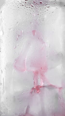 Pouring cherry juice in glass with ice cubes, macro