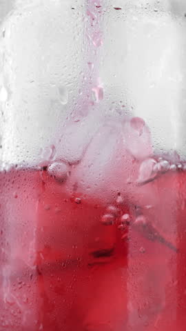 Pouring cherry juice in glass with ice cubes, macro