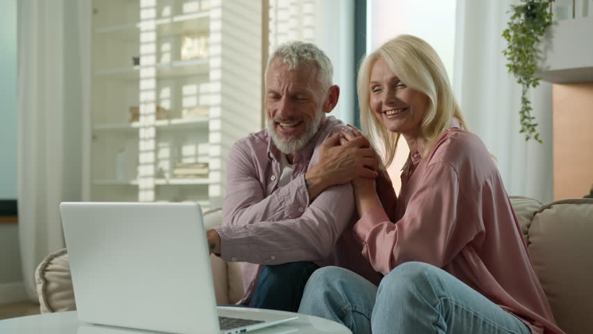 Happy senior family Caucasian couple elderly woman man talking online video call female male using laptop computer pc mature husband wife laugh cuddle hug talk internet virtual chat indoor living room - Powered by Shutterstock - Get 15% off with code: PIKWIZARD15