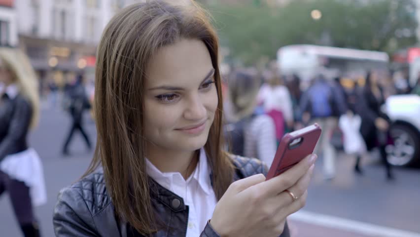 A Young Woman Uses her Smart Phone as She Walks along the City Streets