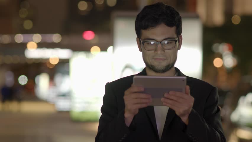 A Gaze of a Man is Fixed upon his Touchpad on a City Nightlife