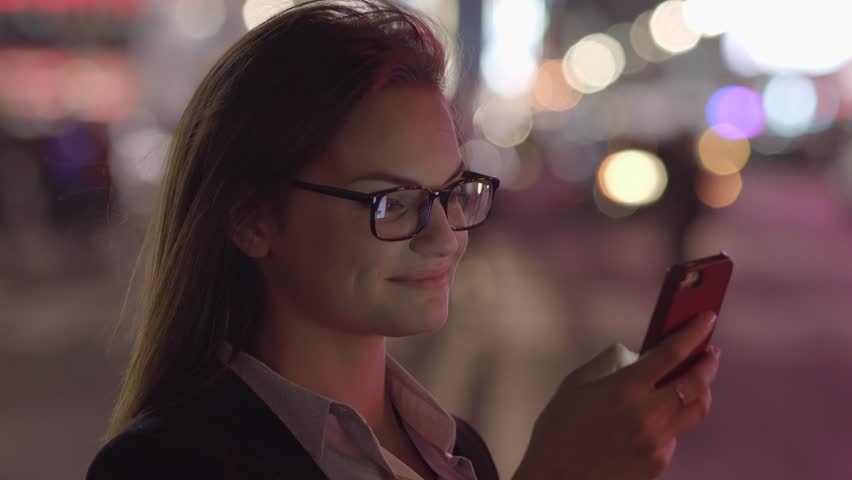 A Young Woman Uses her Smart Phone as She Walks along the City Streets