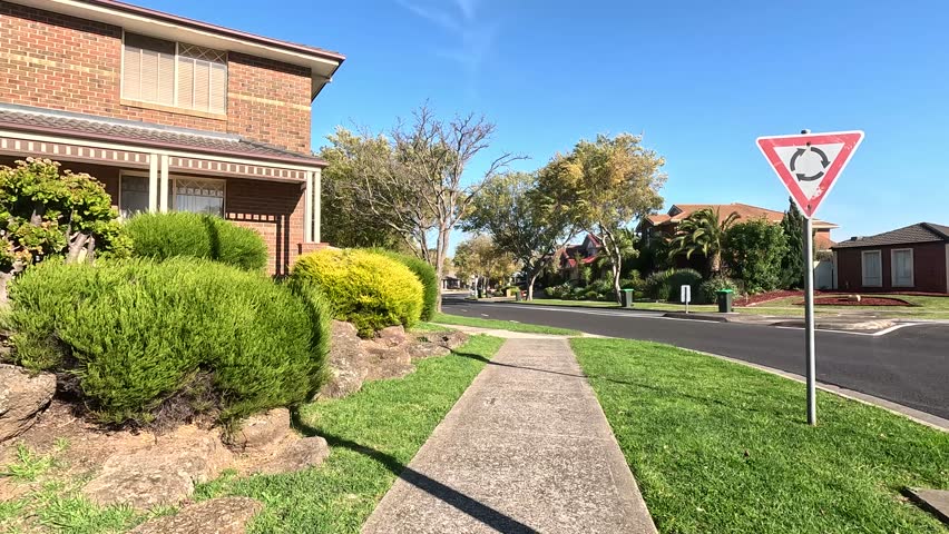 A footpath in a suburban neighborhood with green trees, houses, and front yard gardens. Quiet and Beautiful living environment in Australia’s residential street in a suburb.