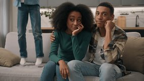 Sad African American family desperate parents hug unhappy mother woman female dissatisfied dad man male sit couch ignore misbehaves little child loud shouting boy active kid son jumping sofa room home - Powered by Shutterstock - Get 15% off with code: PIKWIZARD15