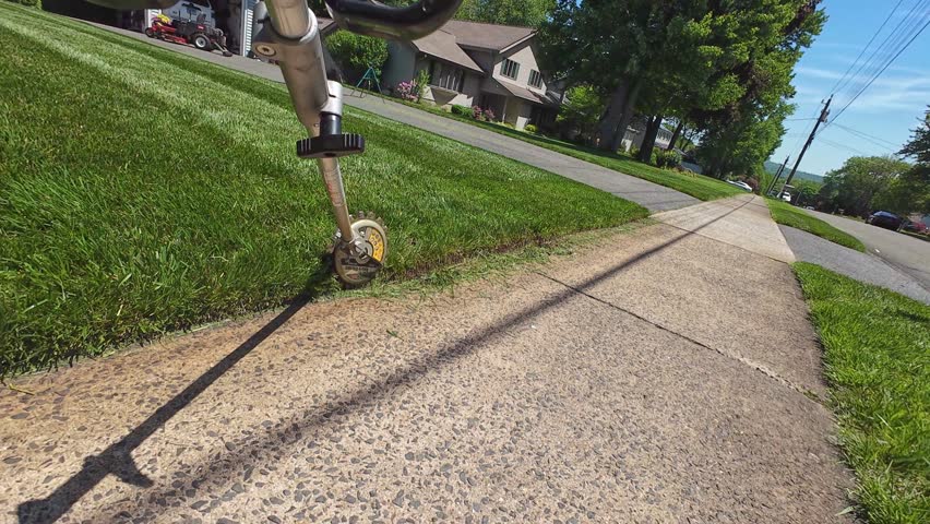 Weed trimmer with rotary scissor attachment trimming grass along residential homeowner property