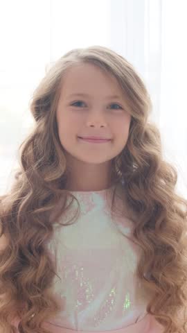 Portrait of a cute little princess with a crown on her head. The girl winks and smiles at the camera. Vertical video.