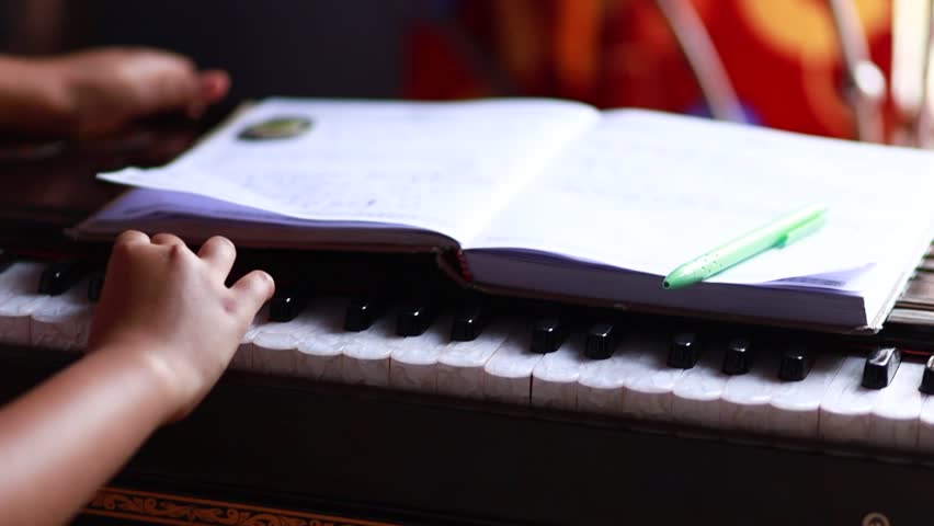 Close up of a hand playing indian classical music instrument harmonium with an open book in front