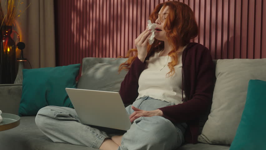 Sick ill Caucasian woman girl female freelancer student health problem influenza flu sickness viral infection allergy sneeze suffer rainy nose blow in napkin sneezing working online laptop home covid