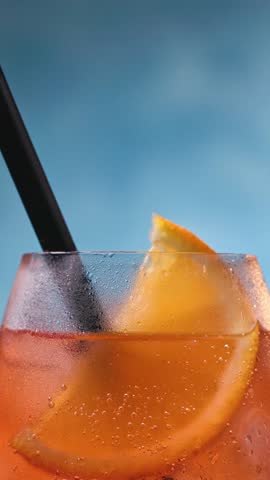 Glass of apperol spritz cocktail with orange slice and straw on blue background. Closeup of summer drink, zoom out