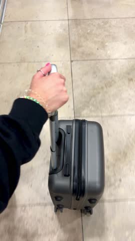 point of view of a hand carrying a wheeled suitcase