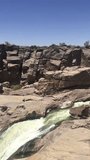Flowing water of the majestic Augrabies Falls in stunning vertical video, showcasing the breathtaking cascade under a clear blue sky during a South African holiday.