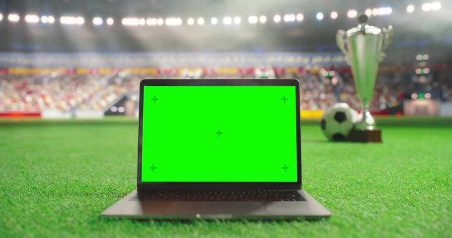 Laptop Computer with a Green Screen Template Standing on a Soccer Pitch with a Trophy and Soccer Ball in the Background. Mock Up Display Suitable for Adding Sports-Themed Digital Content