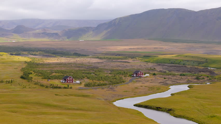 Discover breathtaking aerial views of Iceland beautiful countryside featuring charming houses, lush greenery, a winding river, and majestic mountains. Perfect for nature enthusiasts.