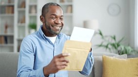 Happy mature african american man reading letter with great news sitting on sofa in living room at home. Joyful smiling senior bearded male is satisfied with pleasant notification, celebrates success - Powered by Shutterstock - Get 15% off with code: PIKWIZARD15