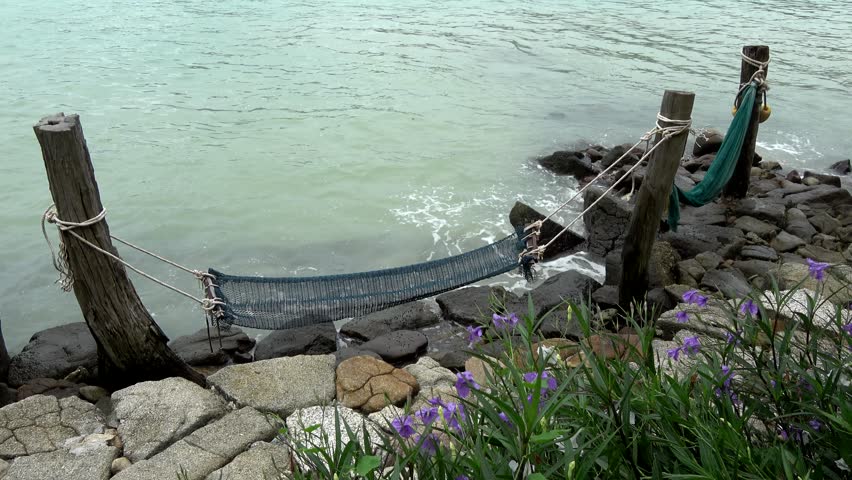 Static view of hammock is a sling made of fabric rope or netting suspended between two or more points used for swinging sleeping or resting at rocky coast showing ocean water in background 4k