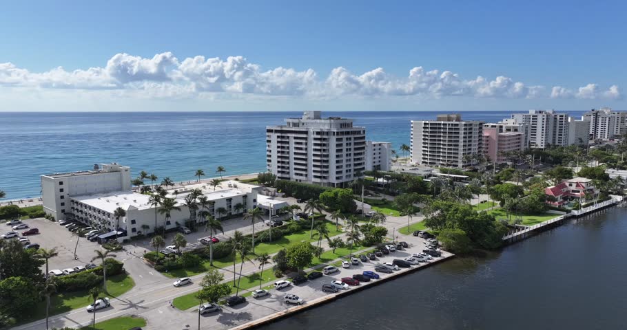 Aerial view frames Boca Raton beachfront condominiums, rooftop pools, palms, Atlantic water, and a calm coastal inlet, 2024.