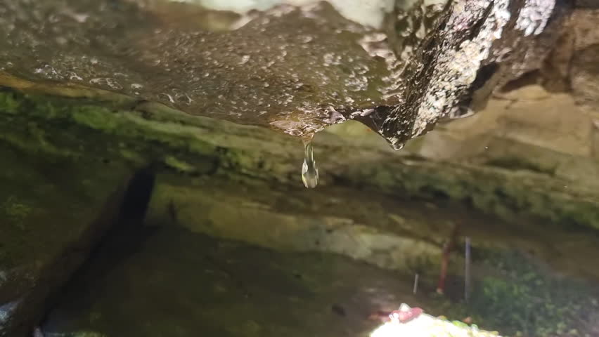 Close-up shot of Water Dripping in Rocky Cave. Water is running down mountainsides, dripping from stone overhang.