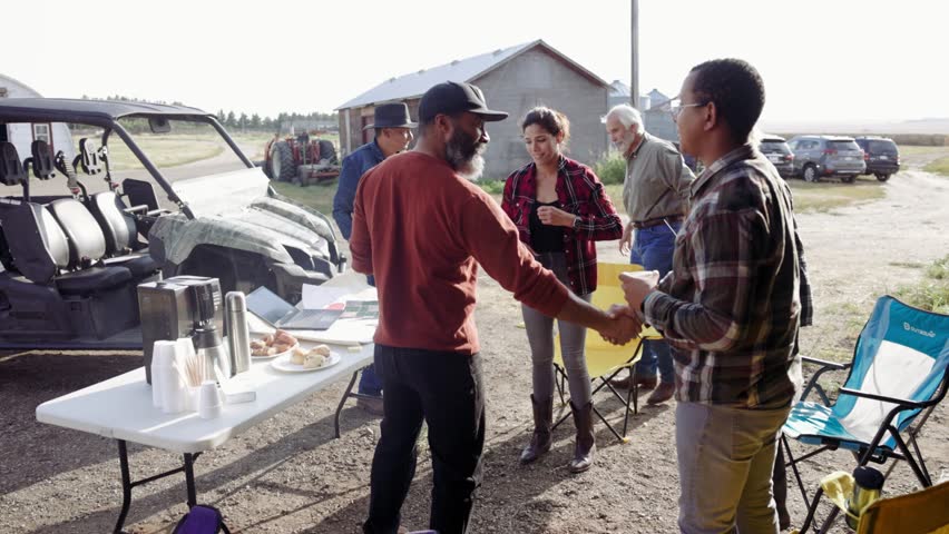 Farmers shaking hands meeting and talking on sunny rural farm