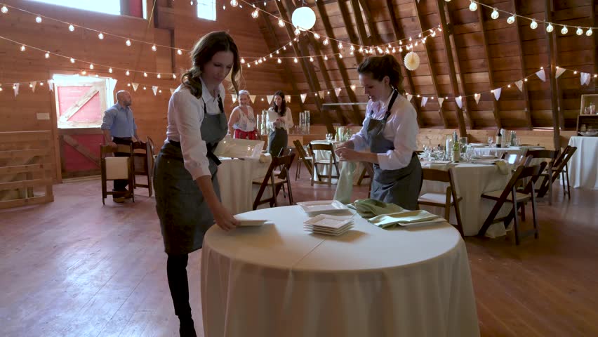 Female caterers setting tables preparing for wedding reception in barn