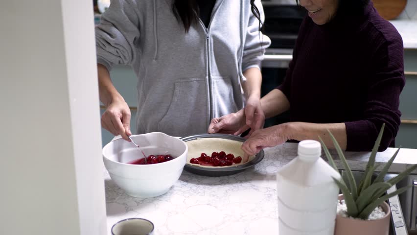 Grandmother and granddaughter baking cherry pie in kitchen at home