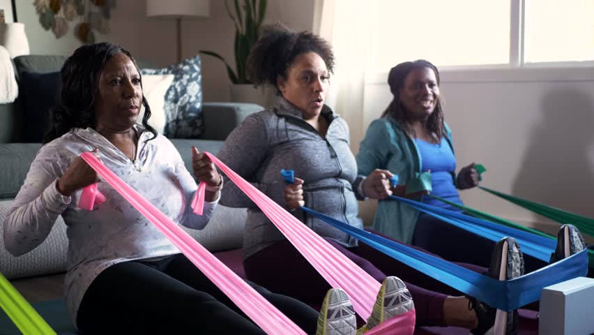 Mature women friends exercising with resistance bands at home