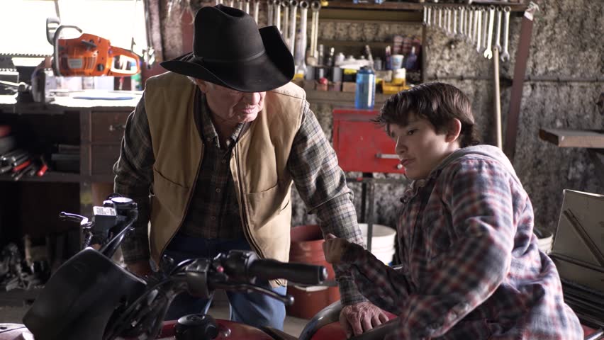 Rancher grandfather and grandson fixing motorcycle in barn workshop