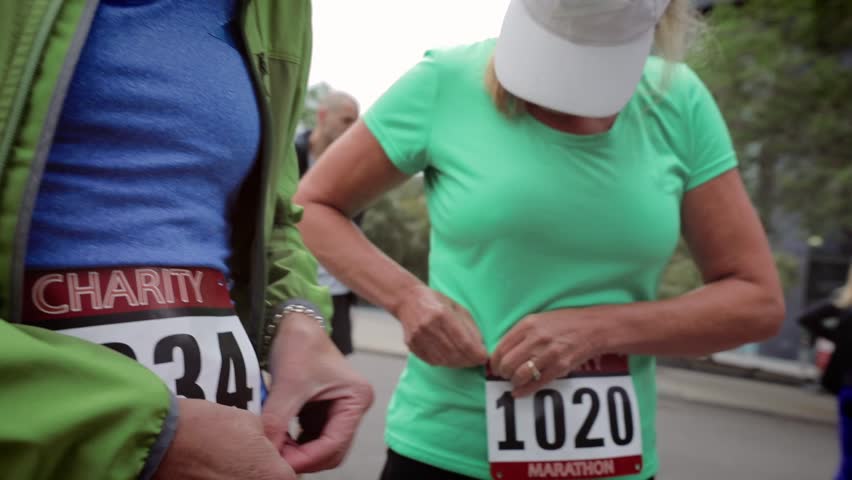 Female runners preparing fastening marathon bibs on urban street