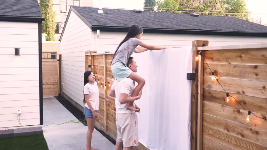 Father and daughters hanging sheet for projection screen in backyard
