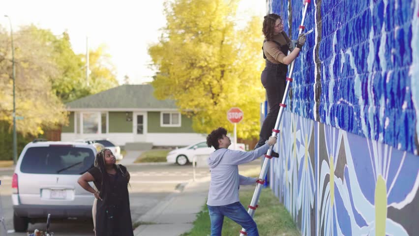 Young volunteers at ladder painting blue mural wall in neighborhood