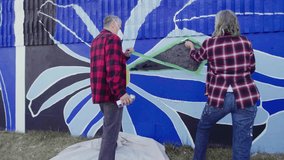 Senior couple removing tape painting blue mural wall - Powered by Shutterstock - Get 15% off with code: PIKWIZARD15