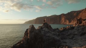 The couple stands on a rocky outcrop overlooking the ocean, holding hands and gazing at the mountainous horizon during sunset. - Powered by Shutterstock - Get 15% off with code: PIKWIZARD15