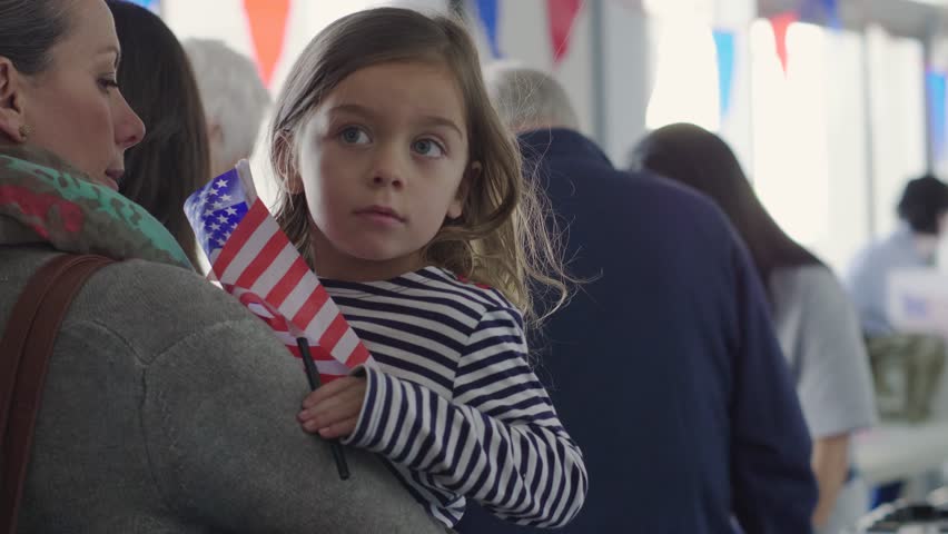 Mother holding daughter with American flag in queue at polling place