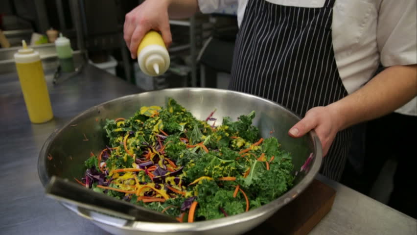 Chef dressing kale salad in commercial kitchen