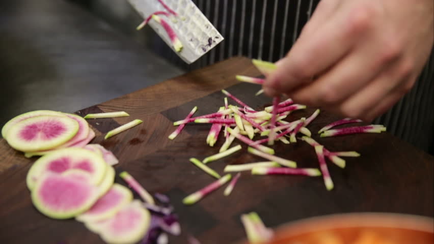 Chef julienning watermelon radishes on cutting board