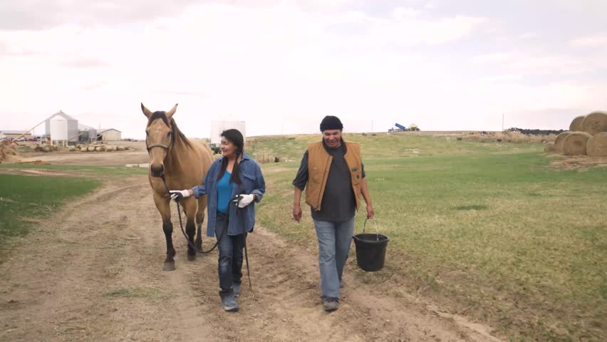 Farmers walking horse along dirt road on rural farm