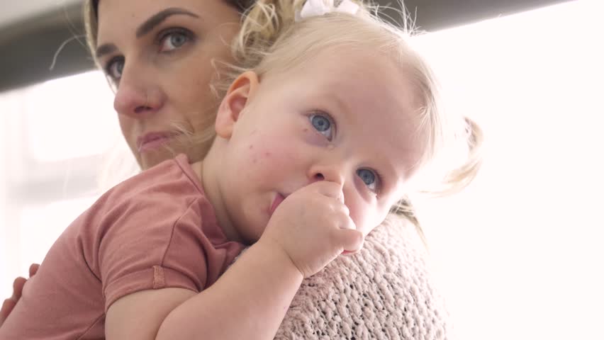 Close up mother holding cute tired toddler daughter sucking thumb