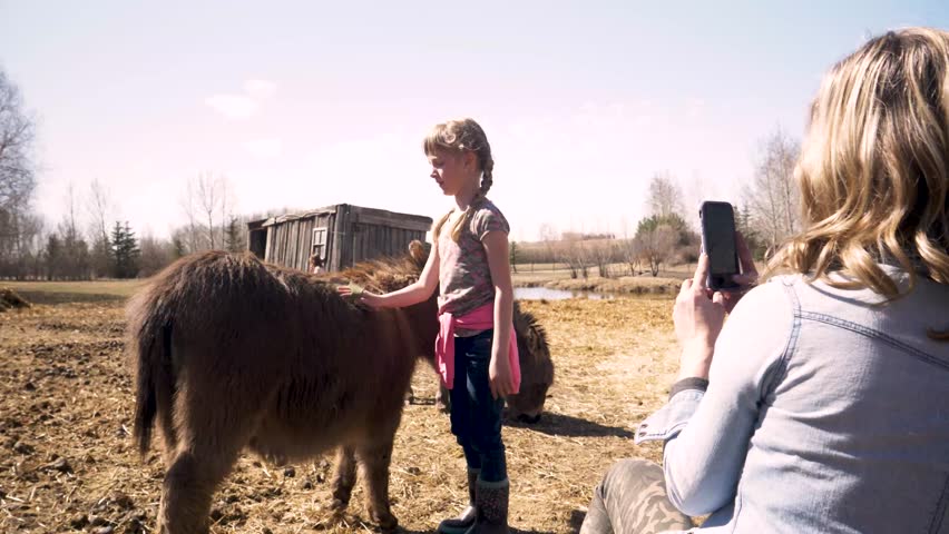 Mother taking photograph of daughter with donkey in farm
