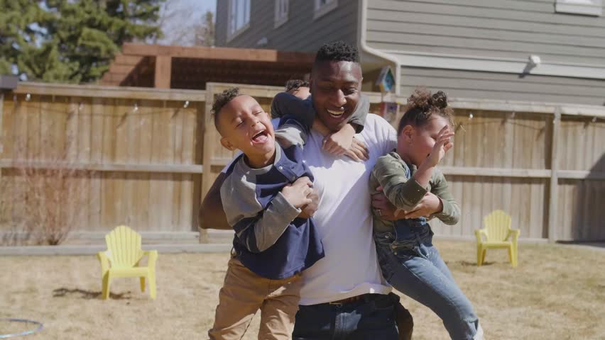 Cheerful family playing and hugging on backyard lawn