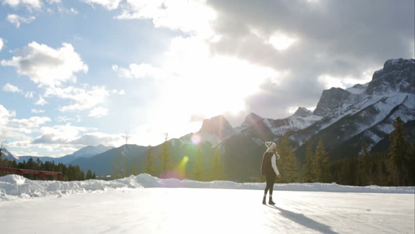 Teenage girl ice skating outdoors below mountains