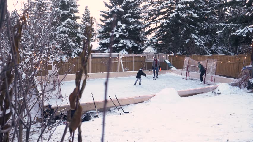 Family playing ice hockey on rink in snowy backyard
