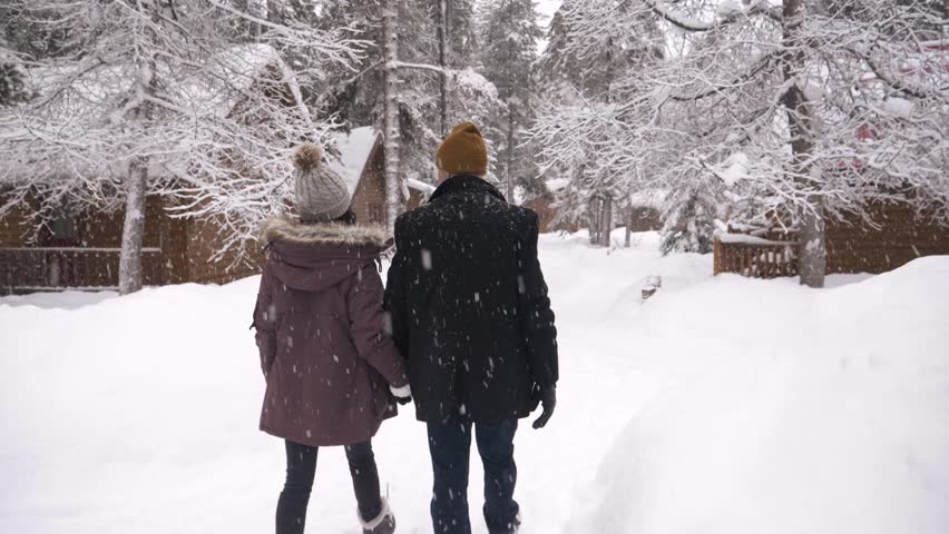 Couple holding hands walking in snow outside winter cabins