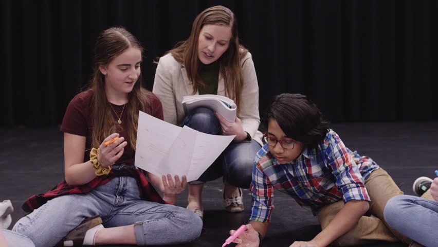 Junior high drama teacher and students rehearsing script on theater stage