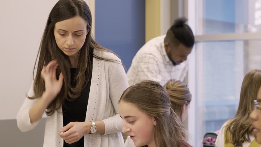 Female junior high teacher helping students doing homework in classroom